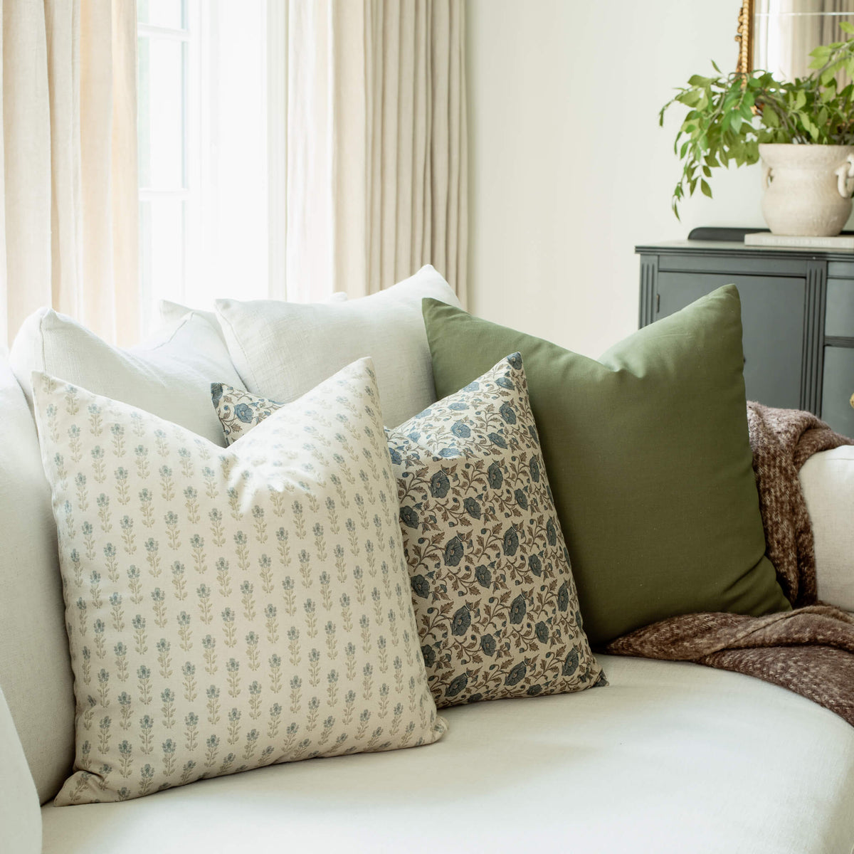 Stella blue floral pillow with navy floral and olive pillows on a sofa