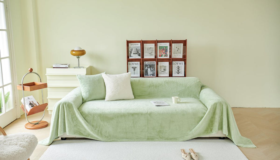 a couch covered in a green blanket with decorative pillows on top of it