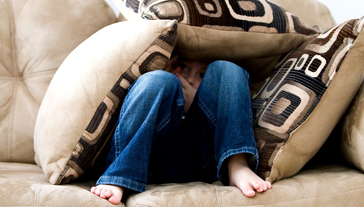 child underneath a bunch of couch pillows