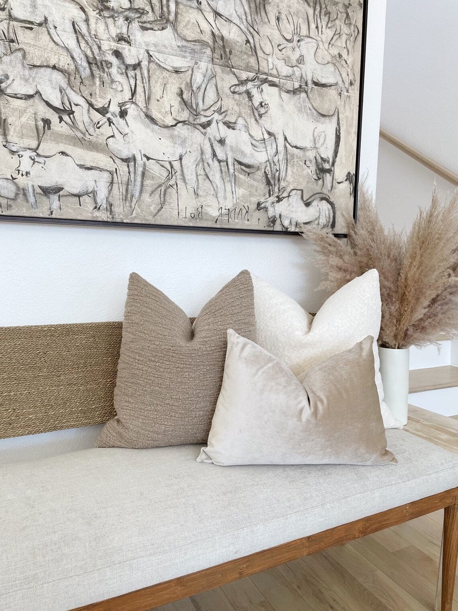 upholstered bench seat with three neutral solid pillow covers with large art above bench.