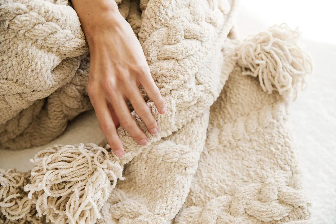Oversized Braided Pom Pom Throw draped across bed in neutral tones
