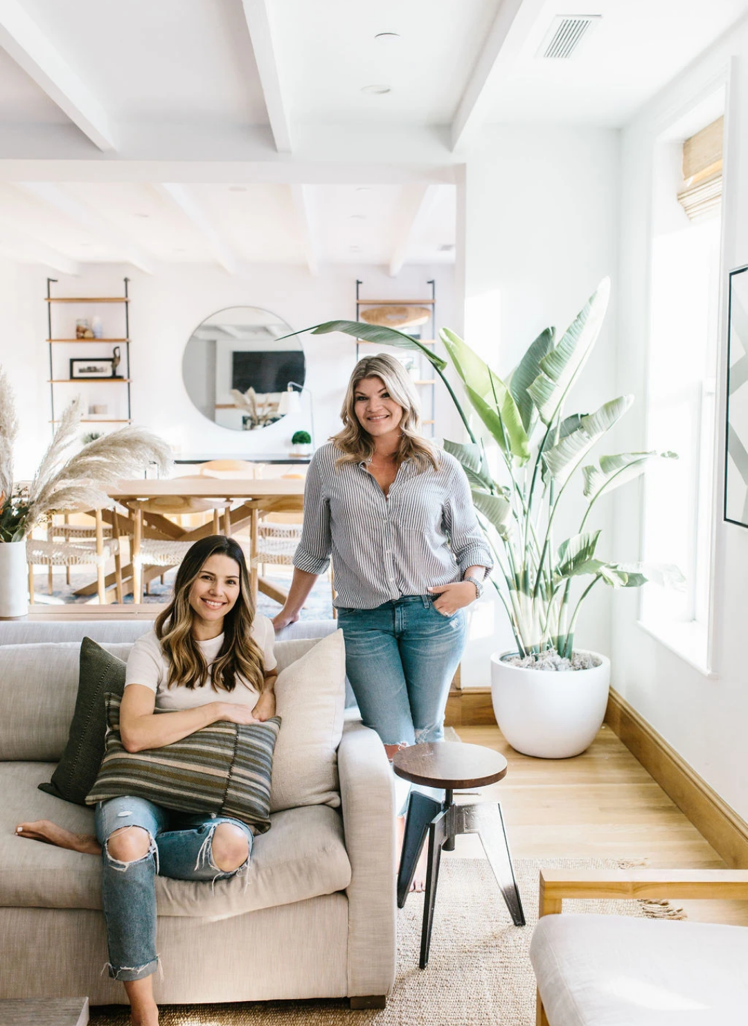 One Affirmation sisters and Co - founders in a modern living room with thextured pillows on neutral sofa with a rug and plants.