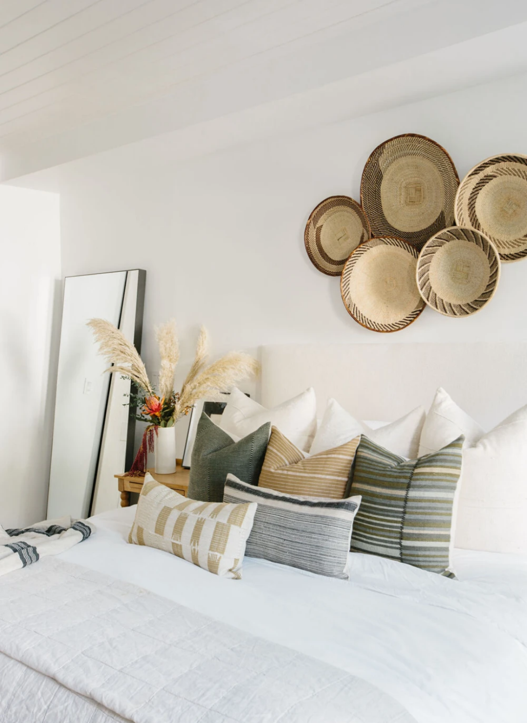 bright and airy bedroom with decorative pillow covers layered with pattern and textures with layered bedding.