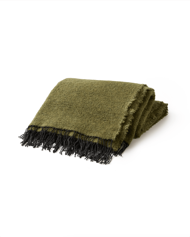 Folded green blanket with black fringes on a white background