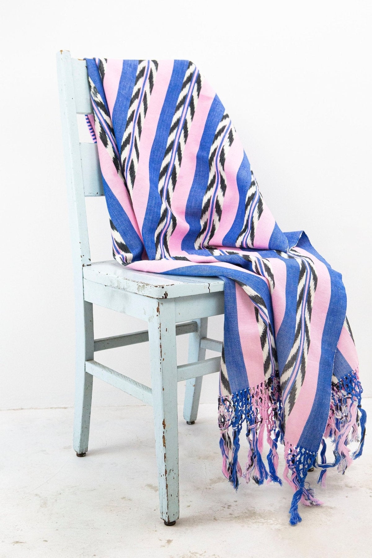 Palm ikat blanket in blue and pink draped over a chair