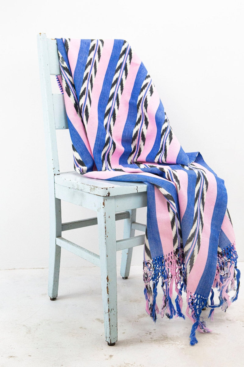 Palm ikat blanket in blue and pink draped over a chair