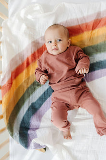 Baby wrapped in Rainbow Connection muslin swaddle blanket