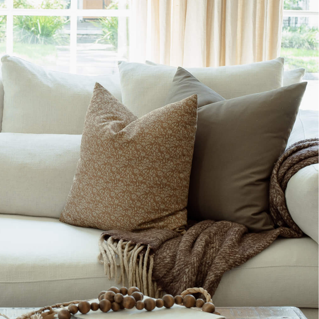 Louisa brown floral pillow with cream and tan block print pillows on an organic modern sofa