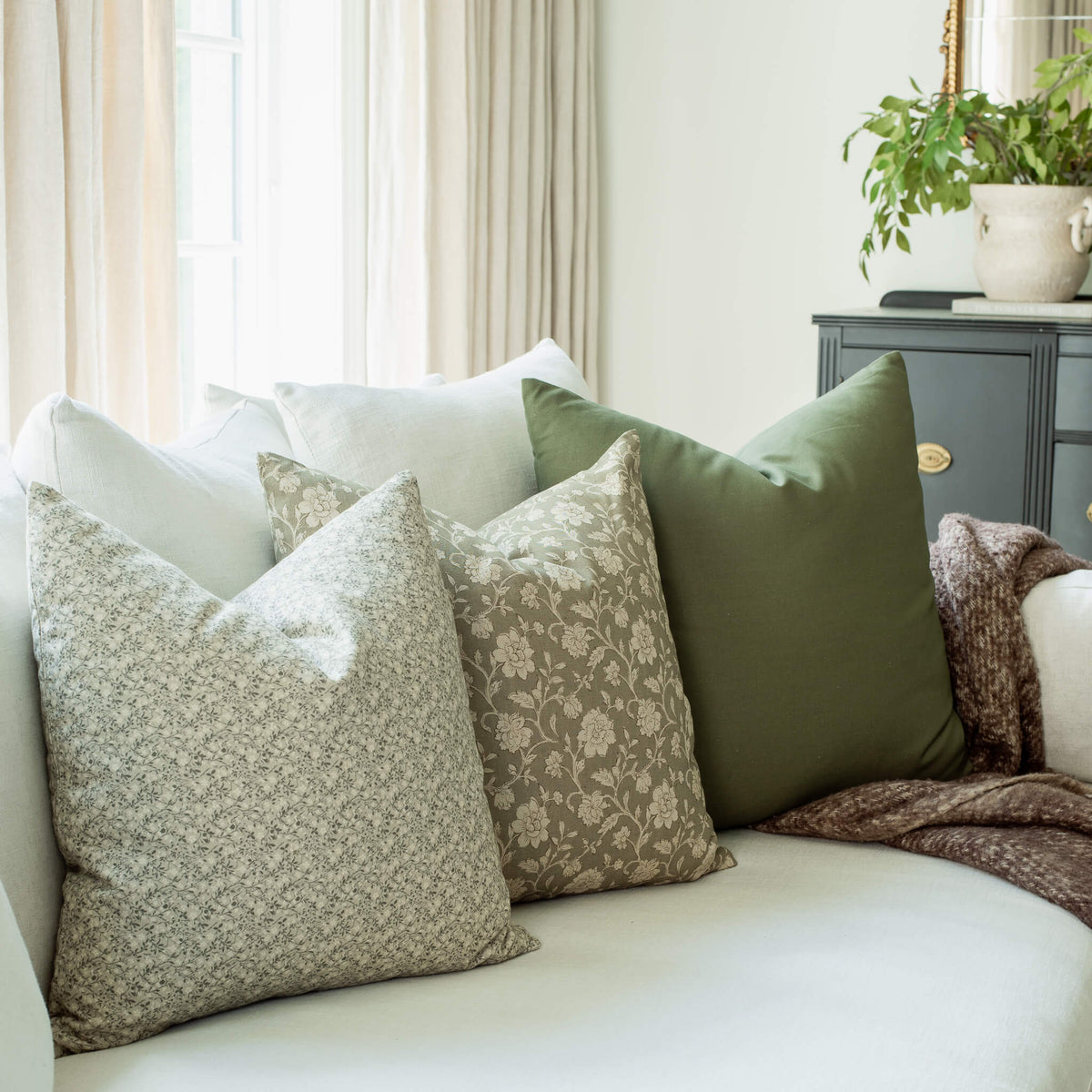 Leme olive pillow with sage floral and taupe botanical pillows on a sofa